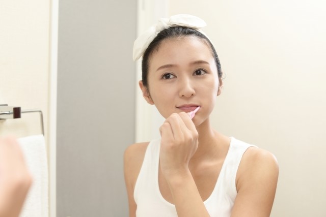 歯磨きをしながら歯ブラシでマッサージをしてほうれい線対策をする女性